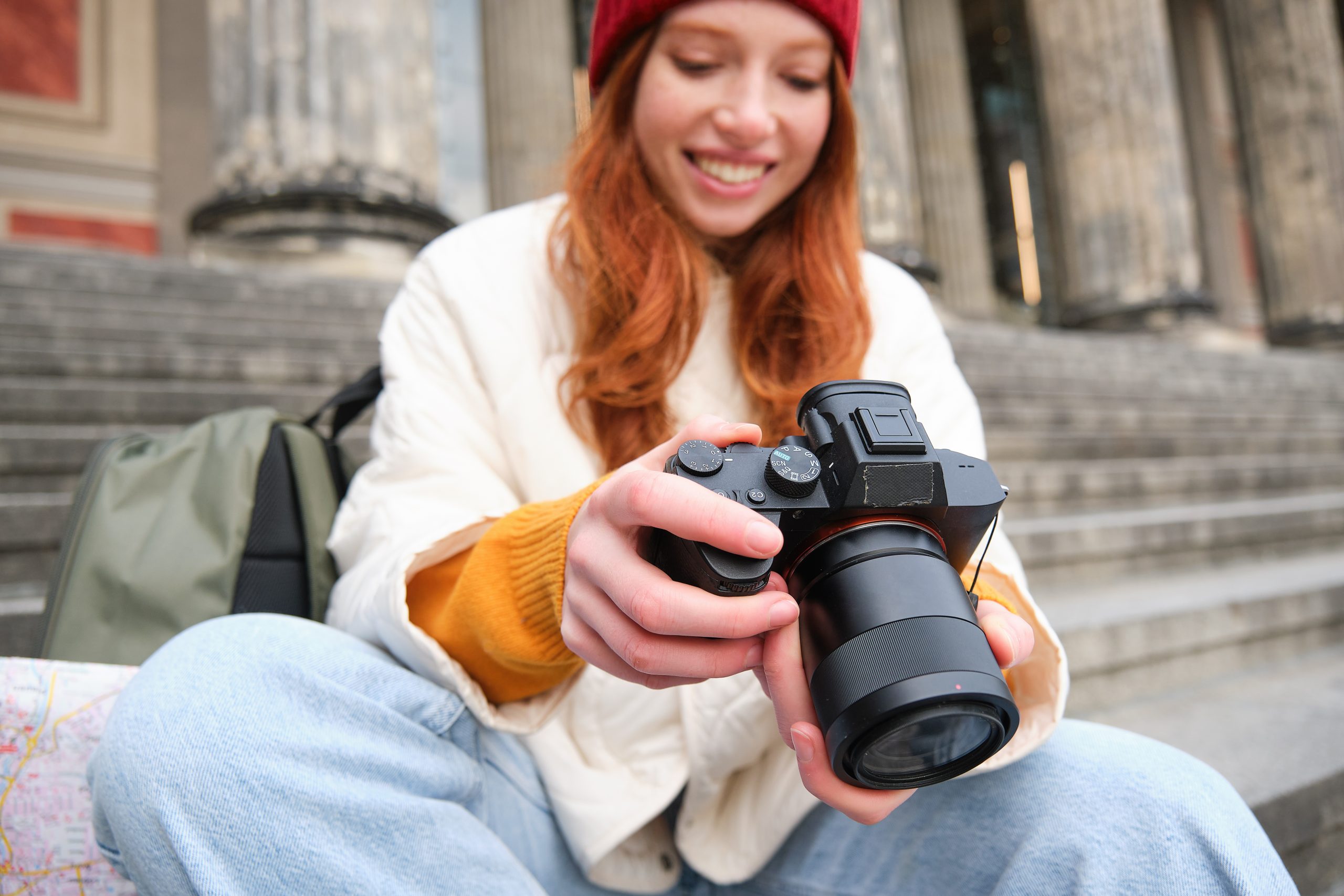 Young student, photographer sits on street stairs and checks her shots on professional camera, taking photos outdoors.